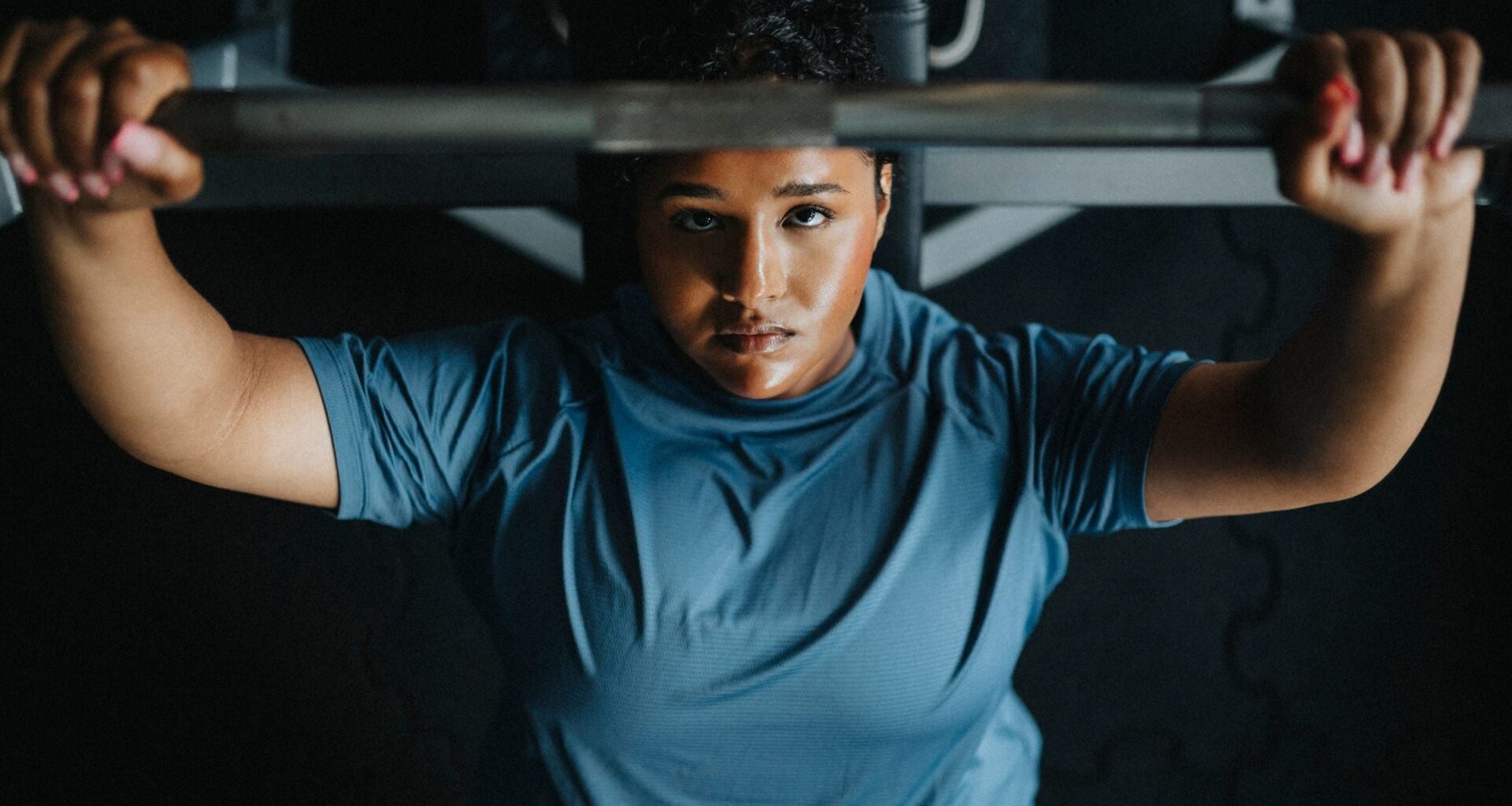 Directly above view of young woman on bench press exercising with barbell at gym