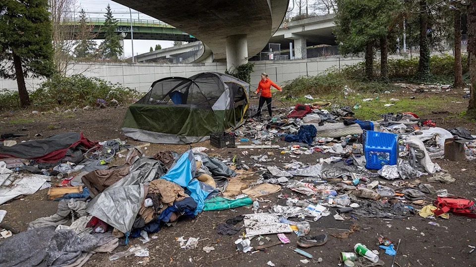Andrea Suarez dismantling a tent at a homeless encampment with garbage piled around in Seattle