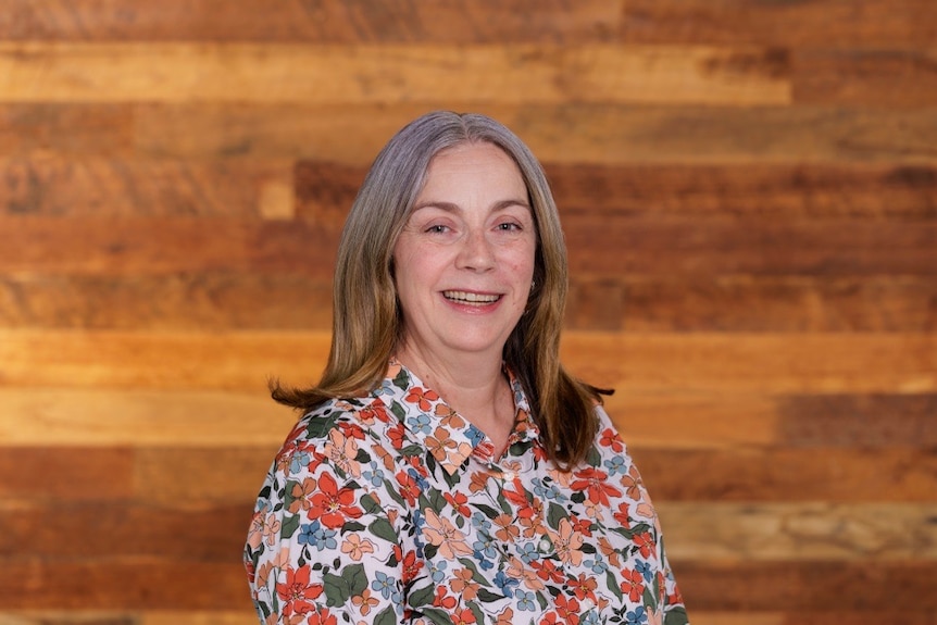 A woman in a floral shirt and mid-length hair smiles at the camera.
