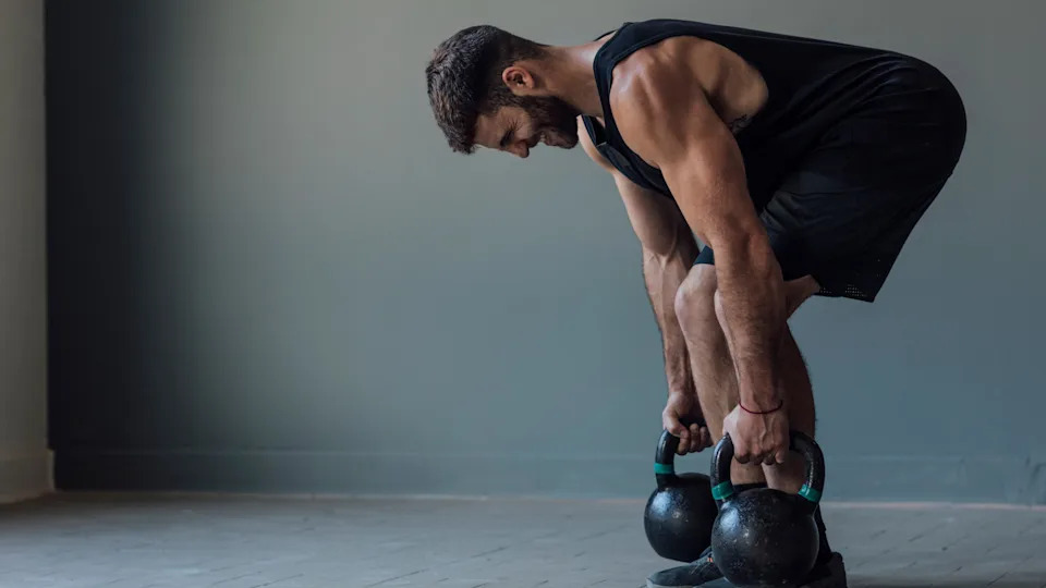 A man performing the gladiator deadlift with two kettlebells