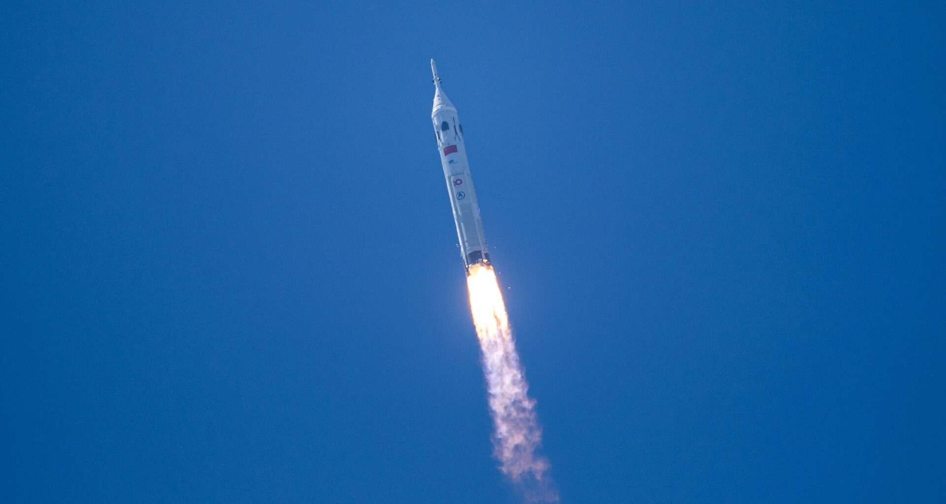 a white rocket launches into a cloudless blue sky