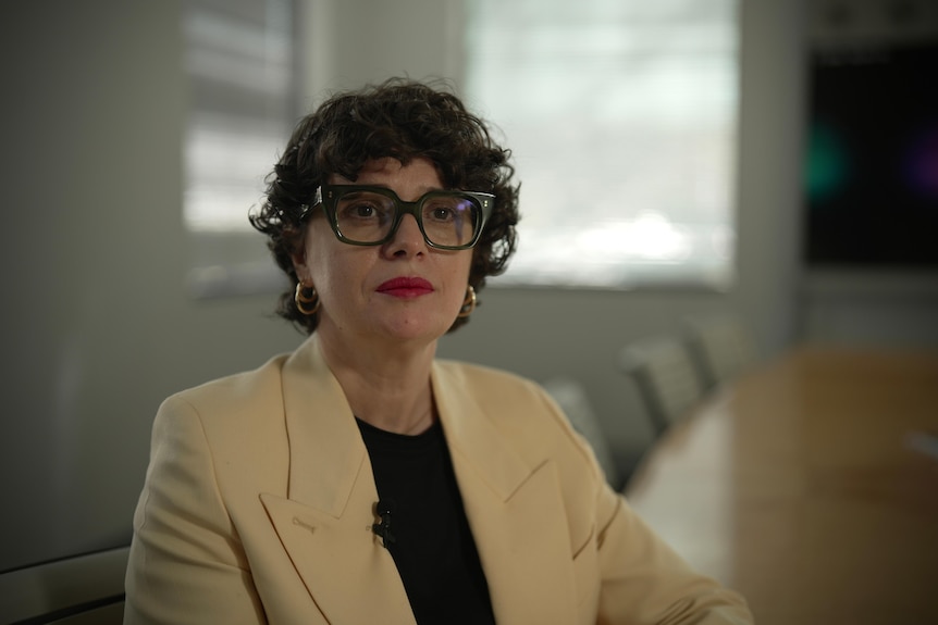 A woman with glasses and brown hair sits at a boardroom table.