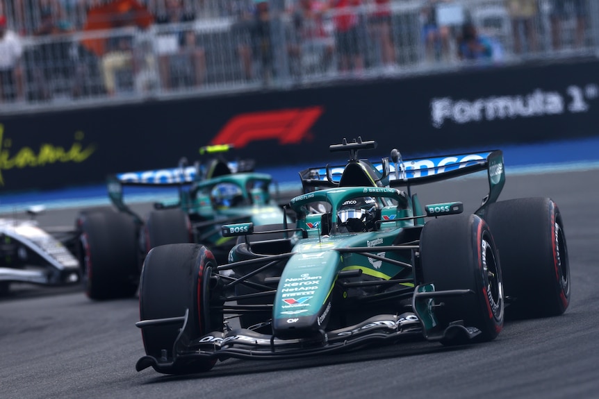 Two F1 cars going around a corner nose to tail.