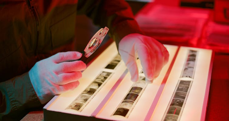 hands with photo negatives on a lightbox, with magnifying glass