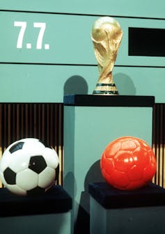 An orange ball and a black and white ball are under a trophy.