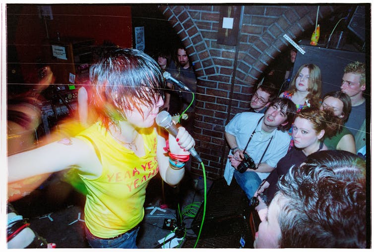 Woman in yellow tshirt performing to a sweaty crowd
