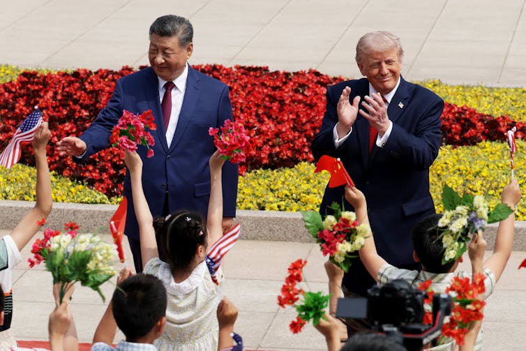 Two men in suits wave and clap hands in front of children.
