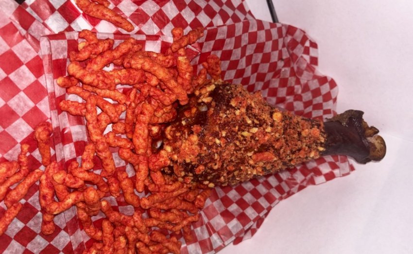 A giant roasted turkey drumstick heavily crusted in bright red crunchy Flamin Hot Cheetos crumbs on the midway.