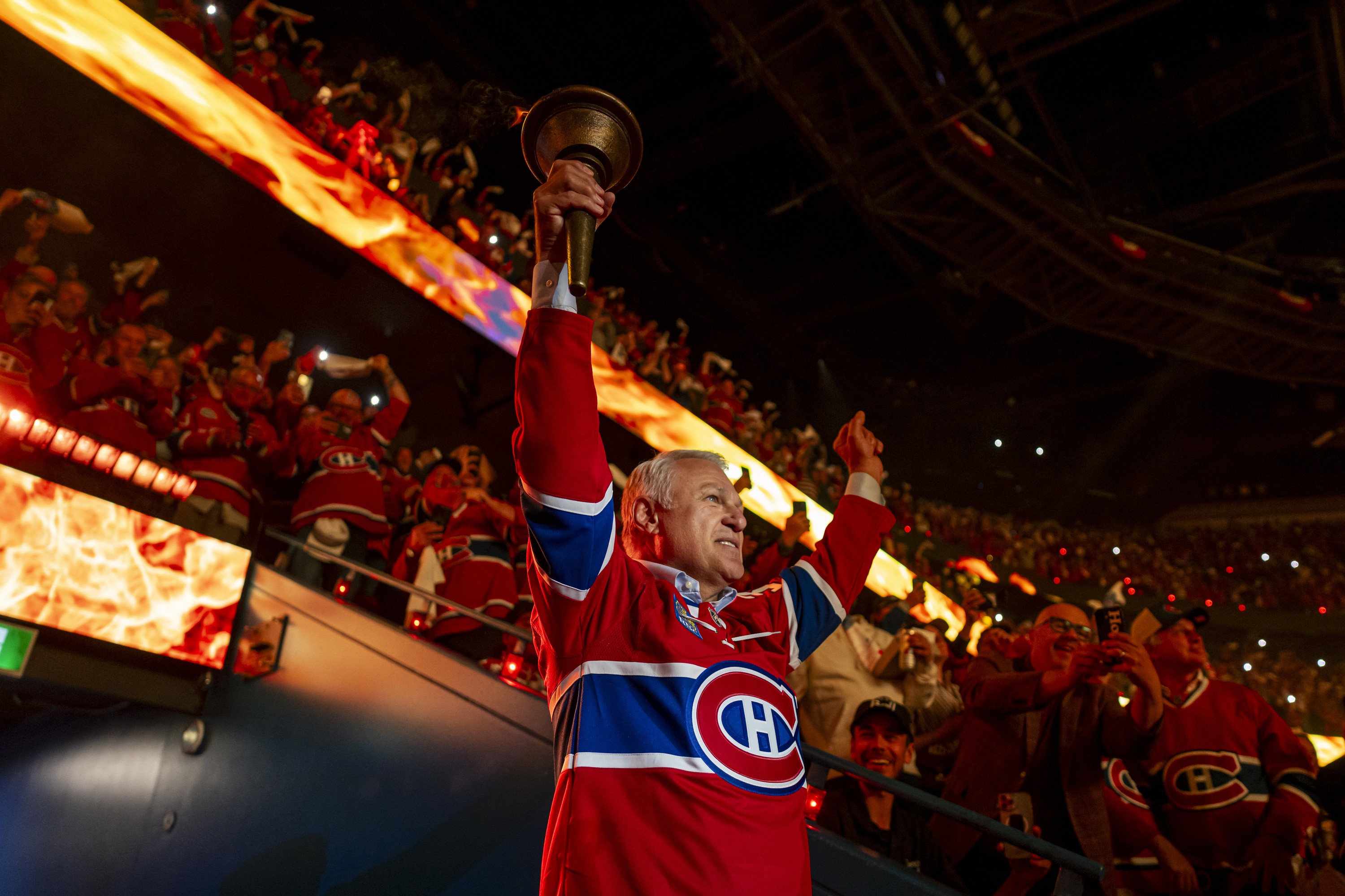 Claude Lemieux holds up a torch at the Bell Centre, with cheering fans in the background.