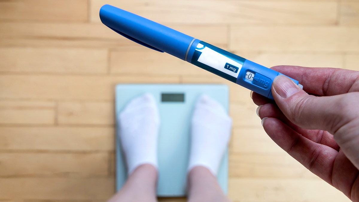 Woman weighing herself on scale holding GLP1 injection in hand