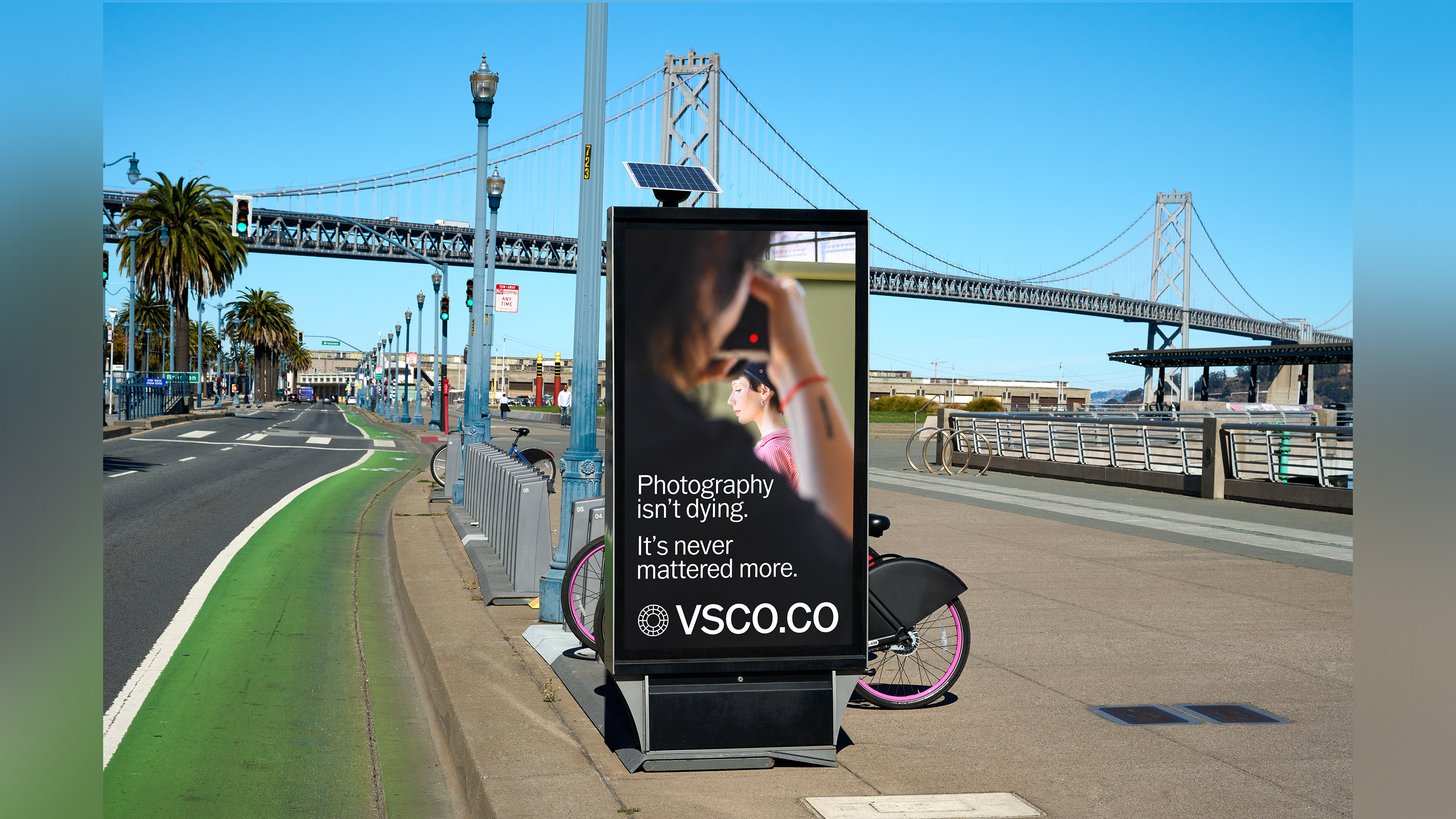 Electronic advertising board at bus stop in US with VSCO ad displayed.