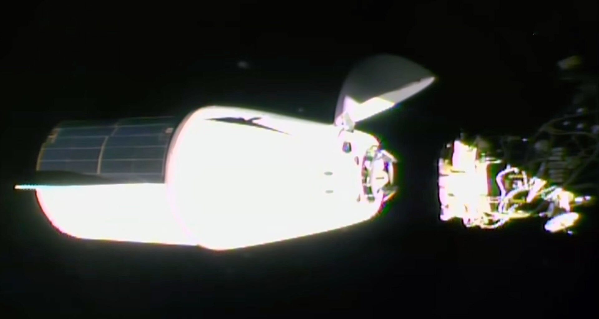 a white spacecraft with a solar array panel covering one half of its trunk approaches docking with a space station