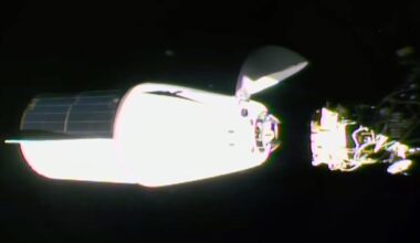 a white spacecraft with a solar array panel covering one half of its trunk approaches docking with a space station