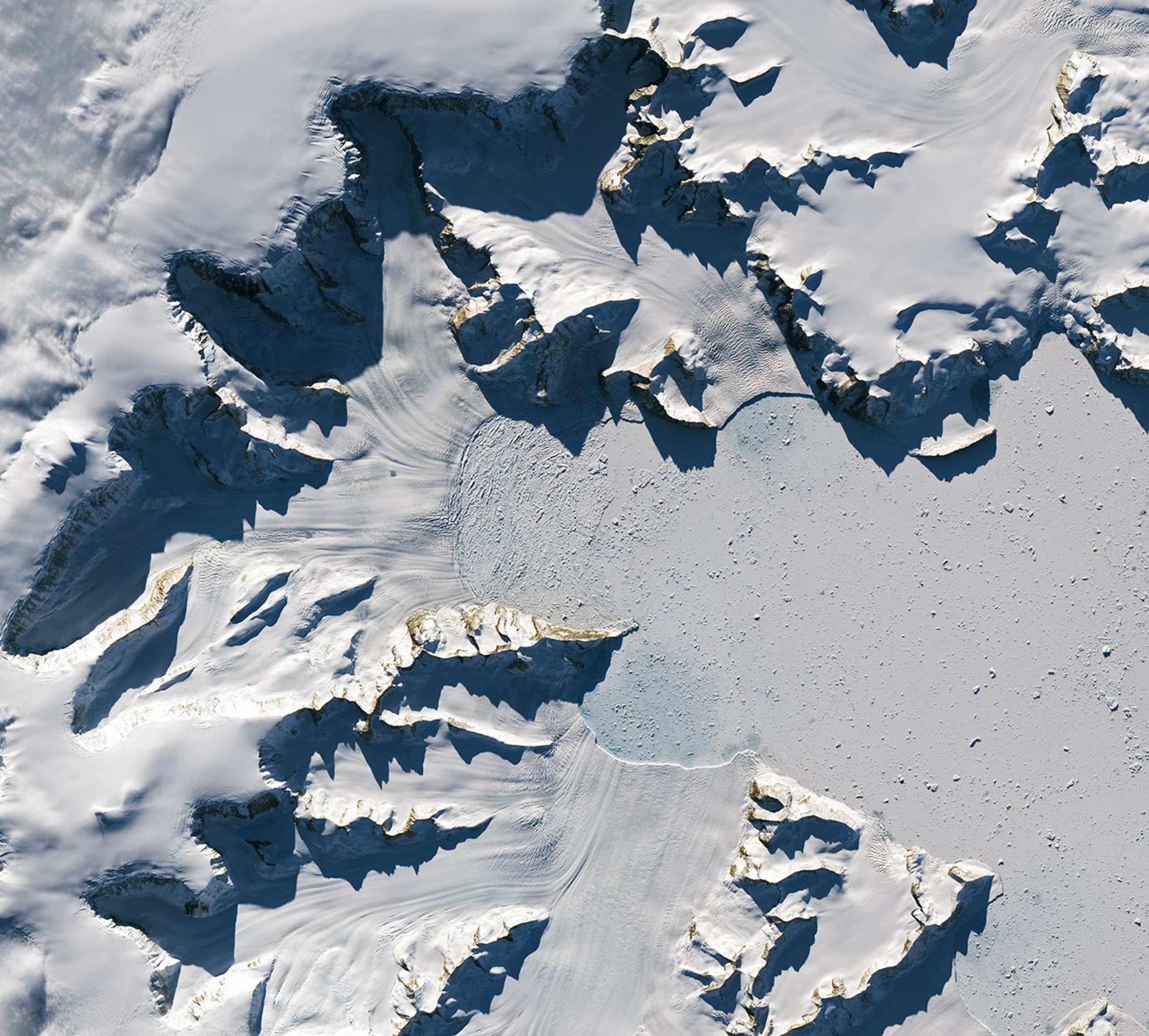 Glaciers flow from the left and bottom sides of the image, terminating much closer to the cliffs than in the previous image.