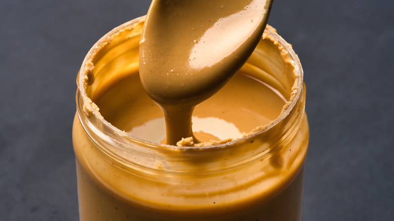 Close-up of a jar of a spoon dripping creamy peanut butter into a jar.