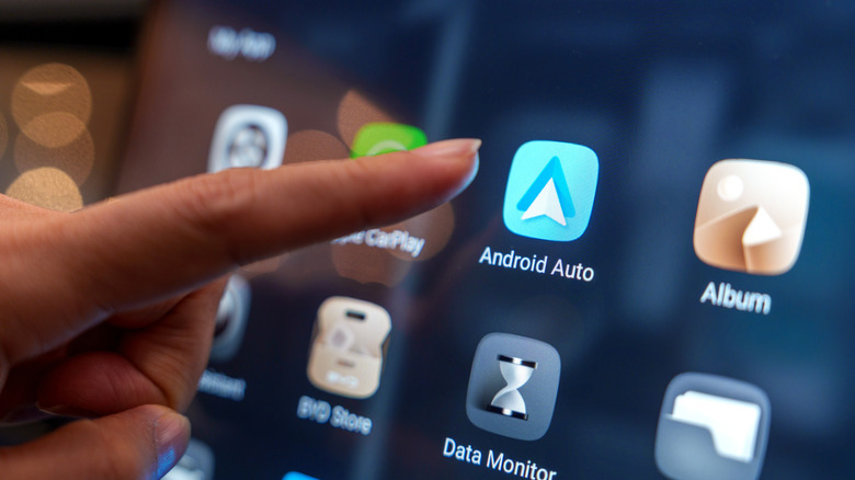 A finger reaching for the Android Auto app on a vehicle display
