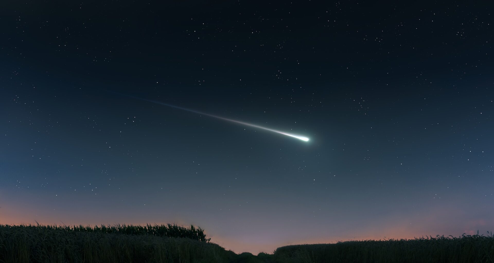 A bright comet streaks across a star-filled night sky above a dark landscape.