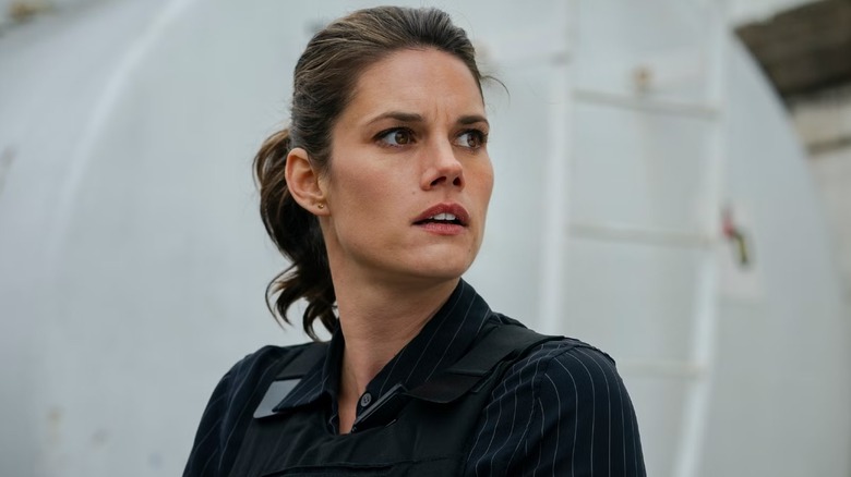 Missy Peregrym as special agent Maggie Bell wearing a black pin-striped long-sleeved blouse and an FBI bulletproof vest, looking off camera with urgency while standing in a white room on FBI