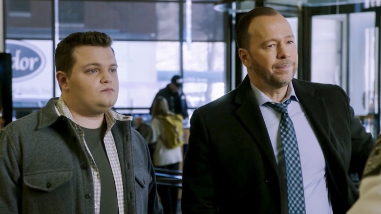 Andrew Terraciano as Sean Reagan, wearing a grey wool jacket and a white and beige checkered shirt with a grey t-shirt underneath, standing next to his father, Donnie Wahlberg as Danny Reagan, wearing a black jacket and light blue collared shirt with a blue checkered tie in Blue Bloods