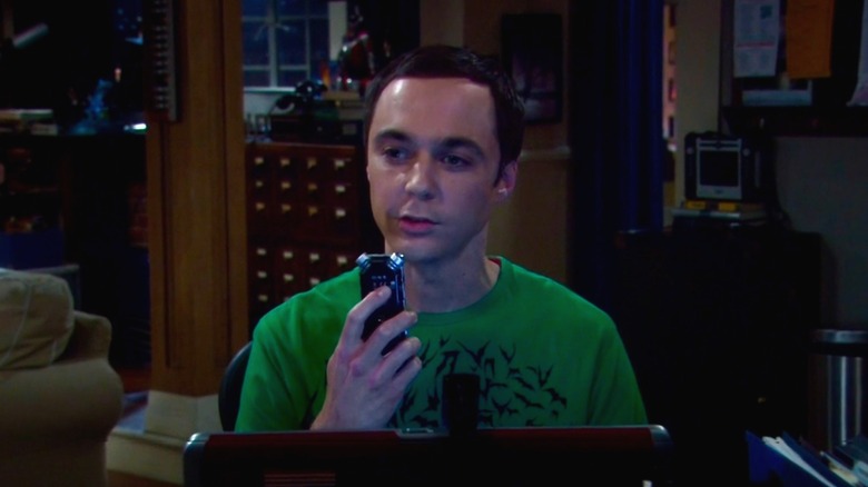 Sheldon Cooper sitting at laptop and speaking into voice recorder