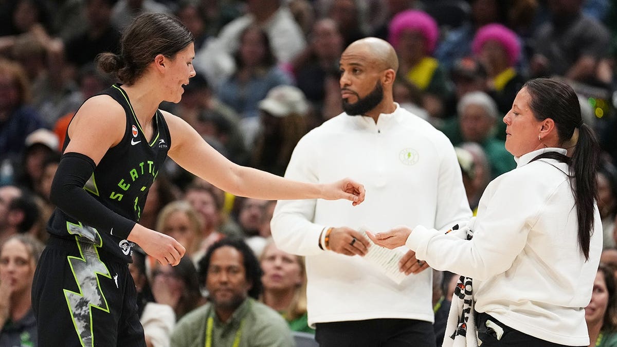 Seattle Storm guard Jade Melbourne handing a piece of her tooth to a staff member during a basketball game