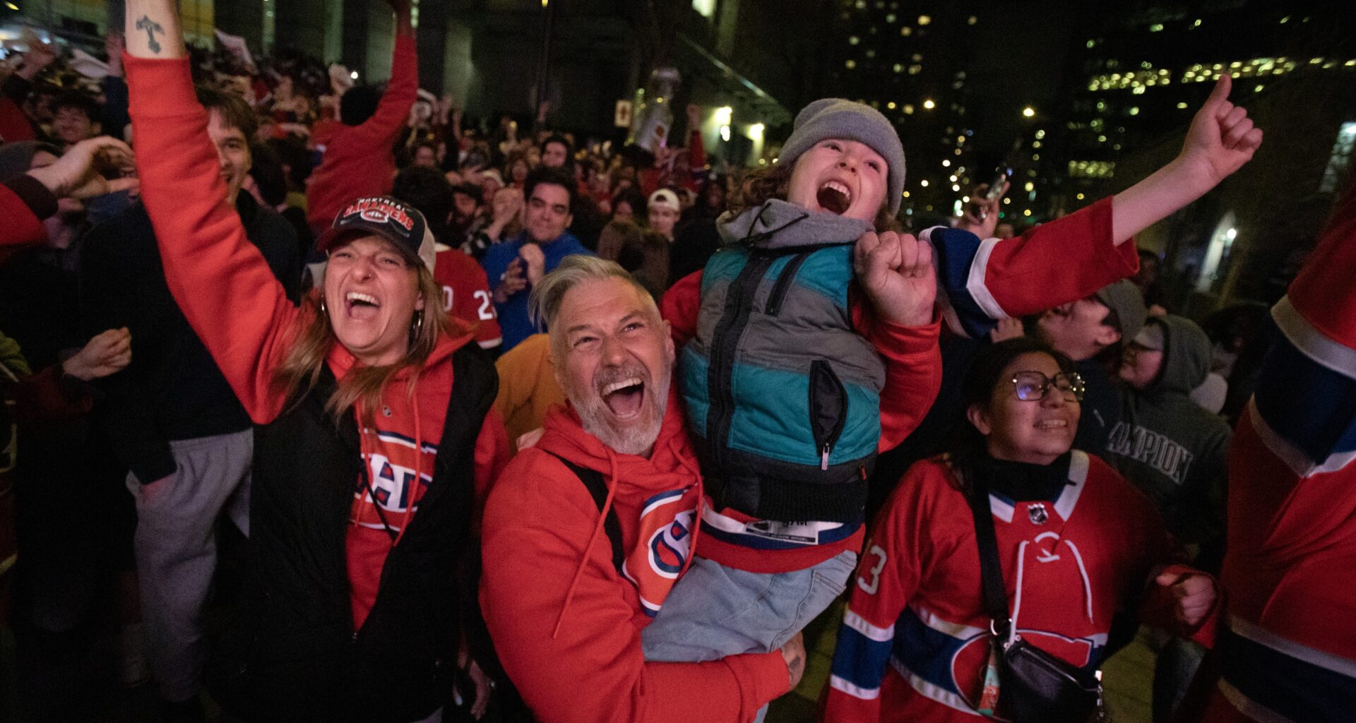 A woman, man and child cheer at the front of a large outdoor crowd of Canadiens fans.