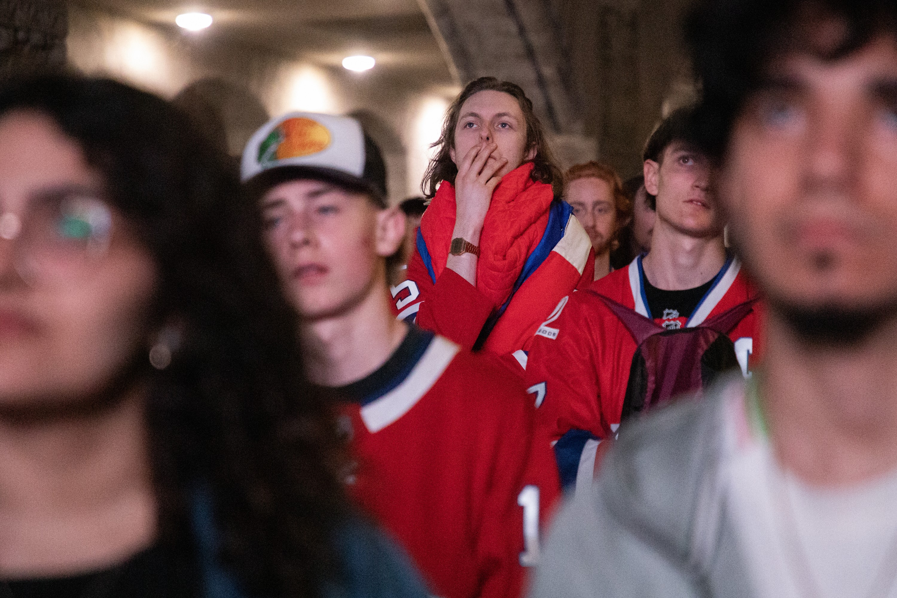 Unhappy Montreal Canadiens fans watch an unseen screen at an outdoor watch party.