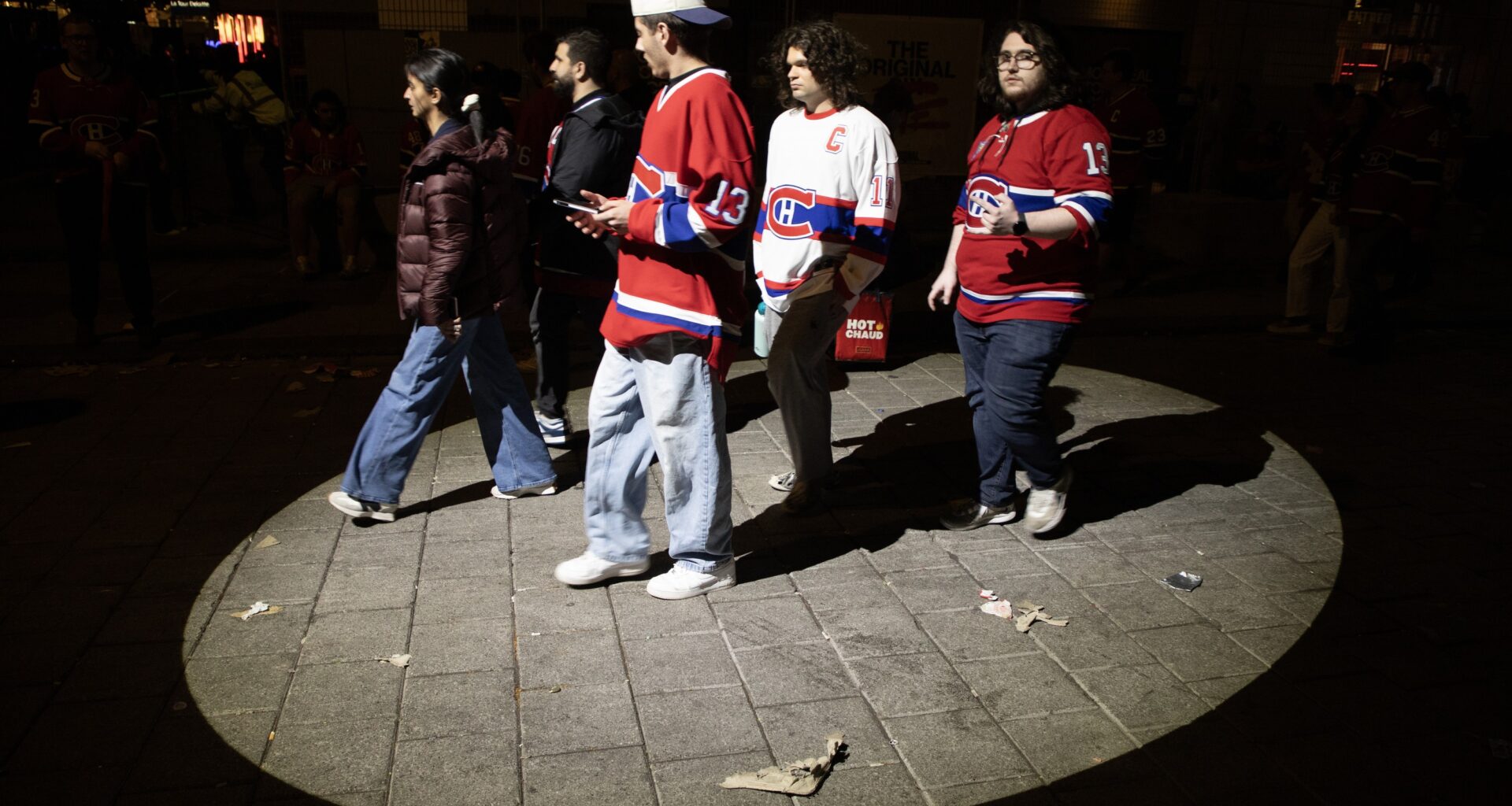 Five Canadiens fans walk through an illuminated circle of pavement at night.