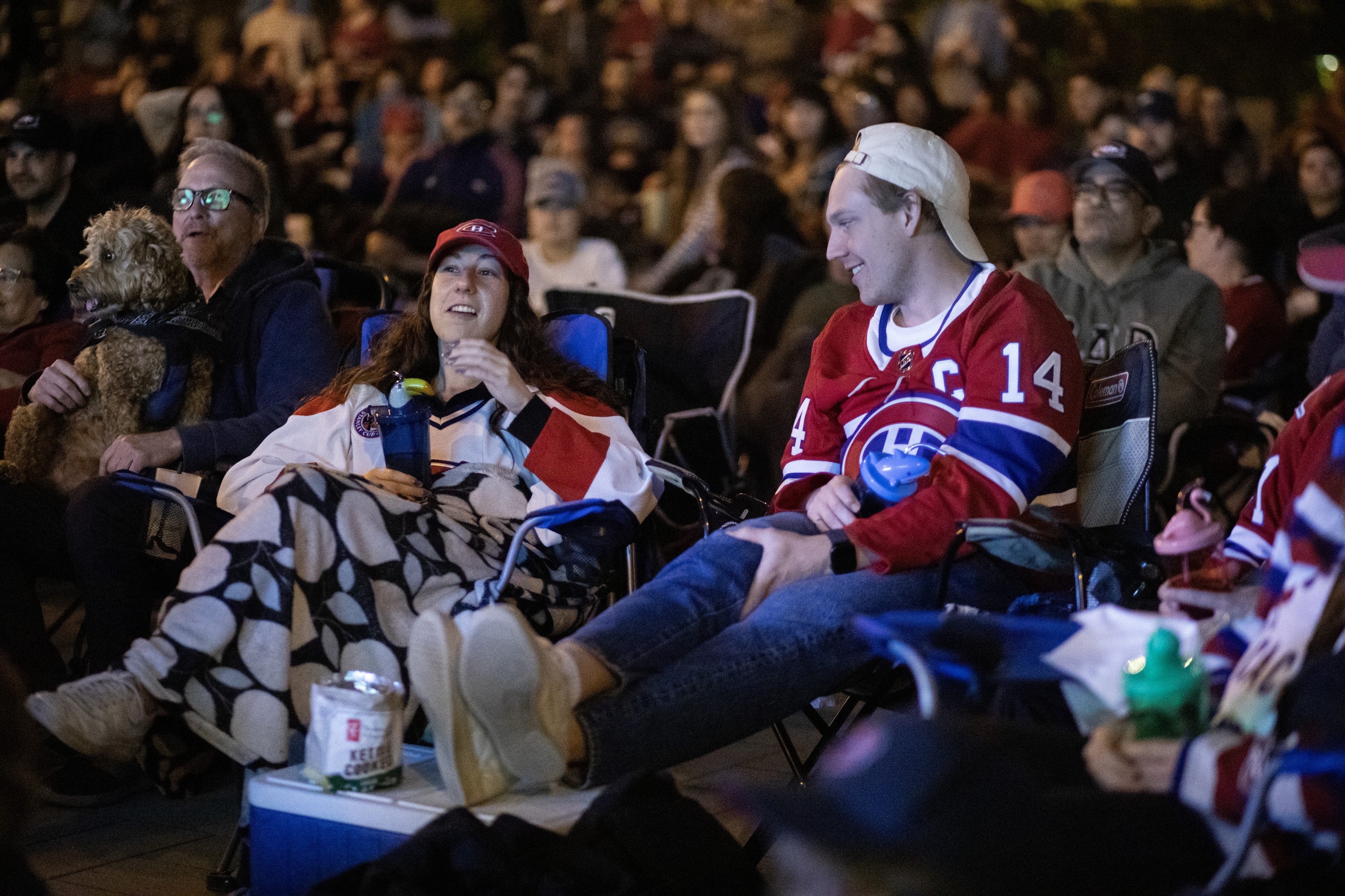 A woman and man in Canadiens gear are at the forefront of a crowd at an outdoor watch party.