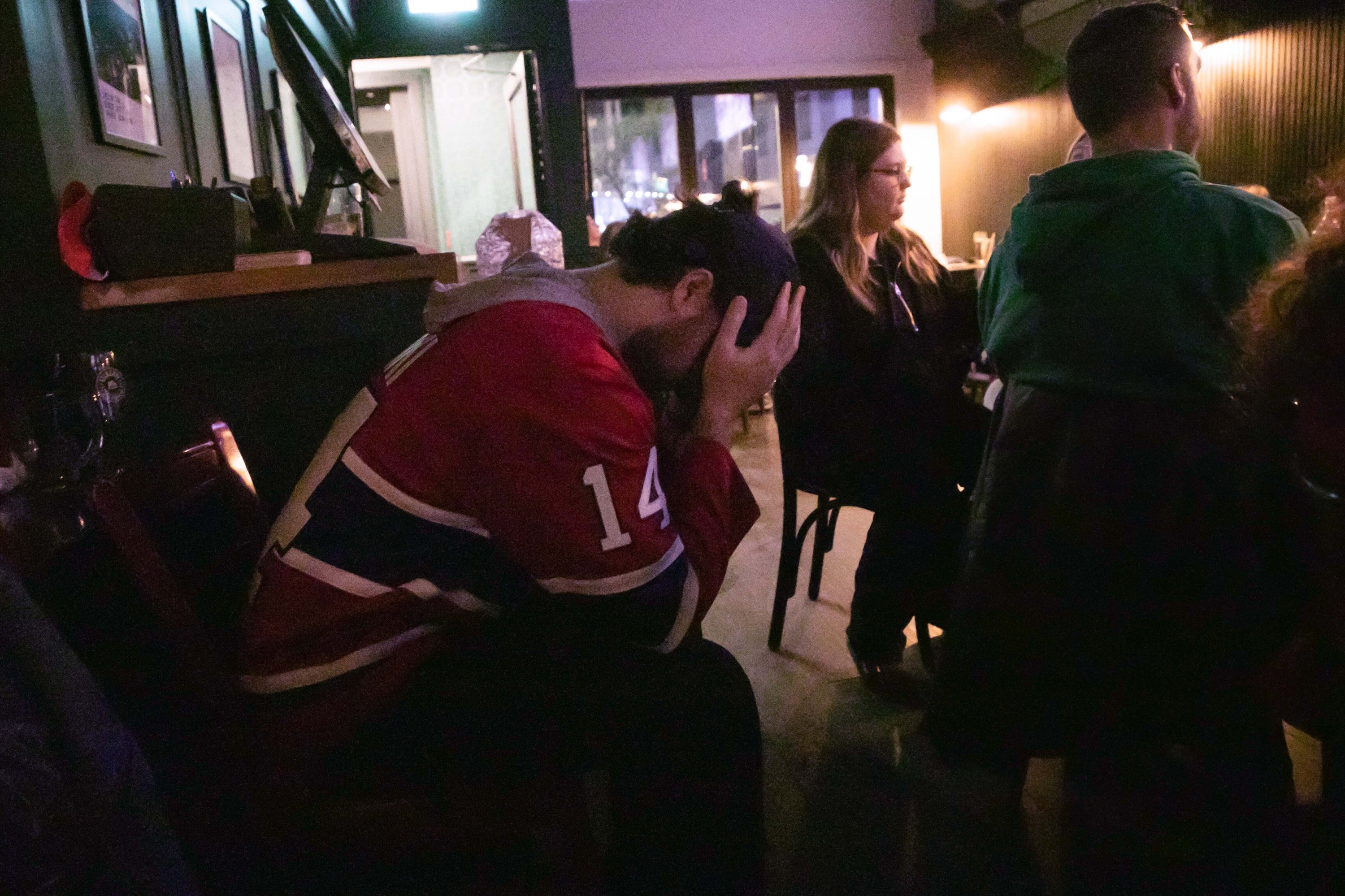 Hockey fan hangs his head down and covers his face his hands watching a game in a bar. 