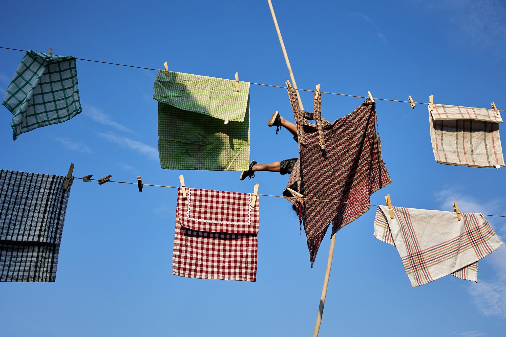 A candid street photograph by Janusz Jurek of textiles hanging on a drying line and someone's legs sticking out from behind one of the pieces