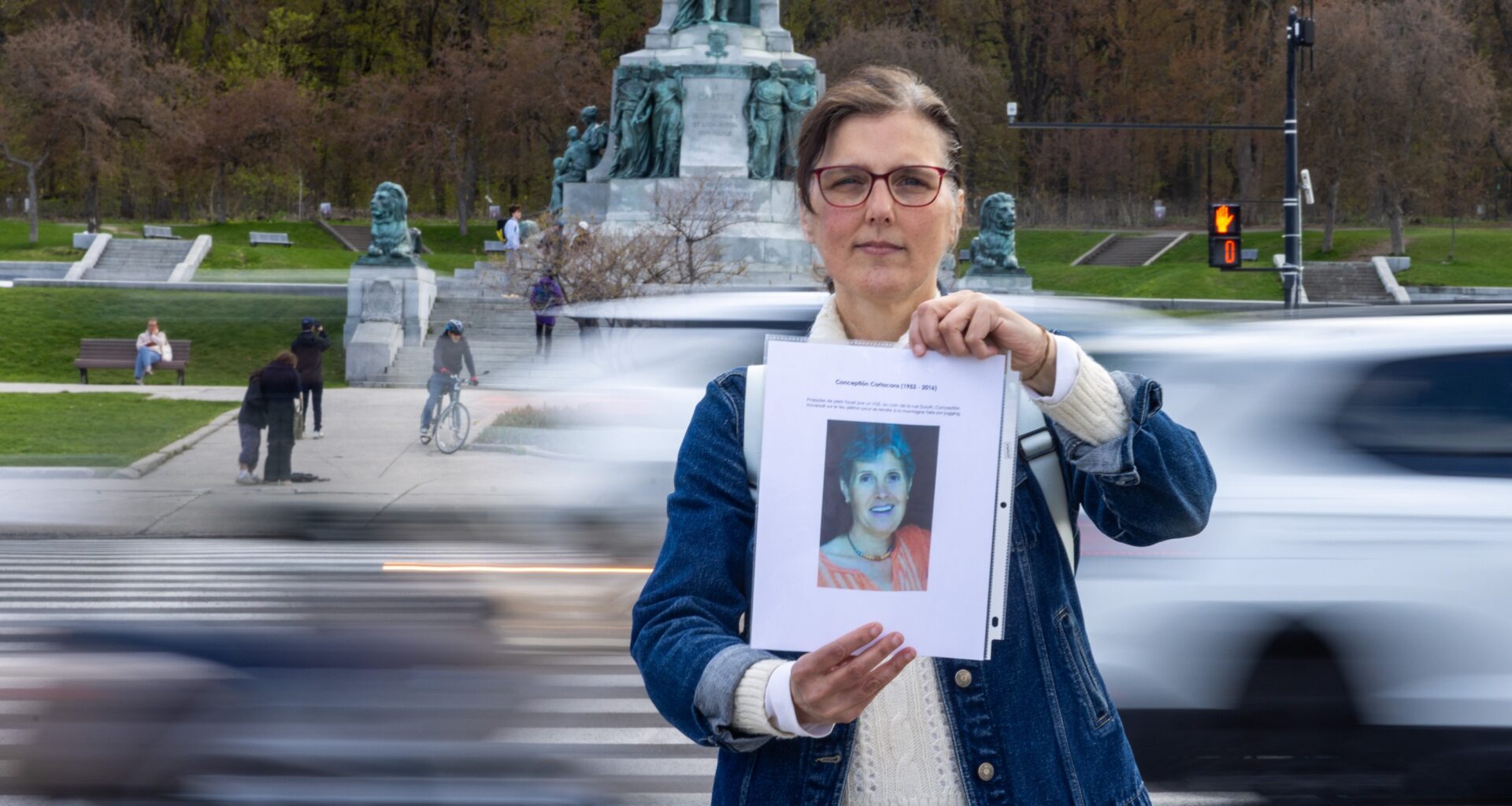 Julie Labelle-Patenaude holds up a picture of Concepción Cortacans against backdrop of monument on Parc Ave. with cars driving by.