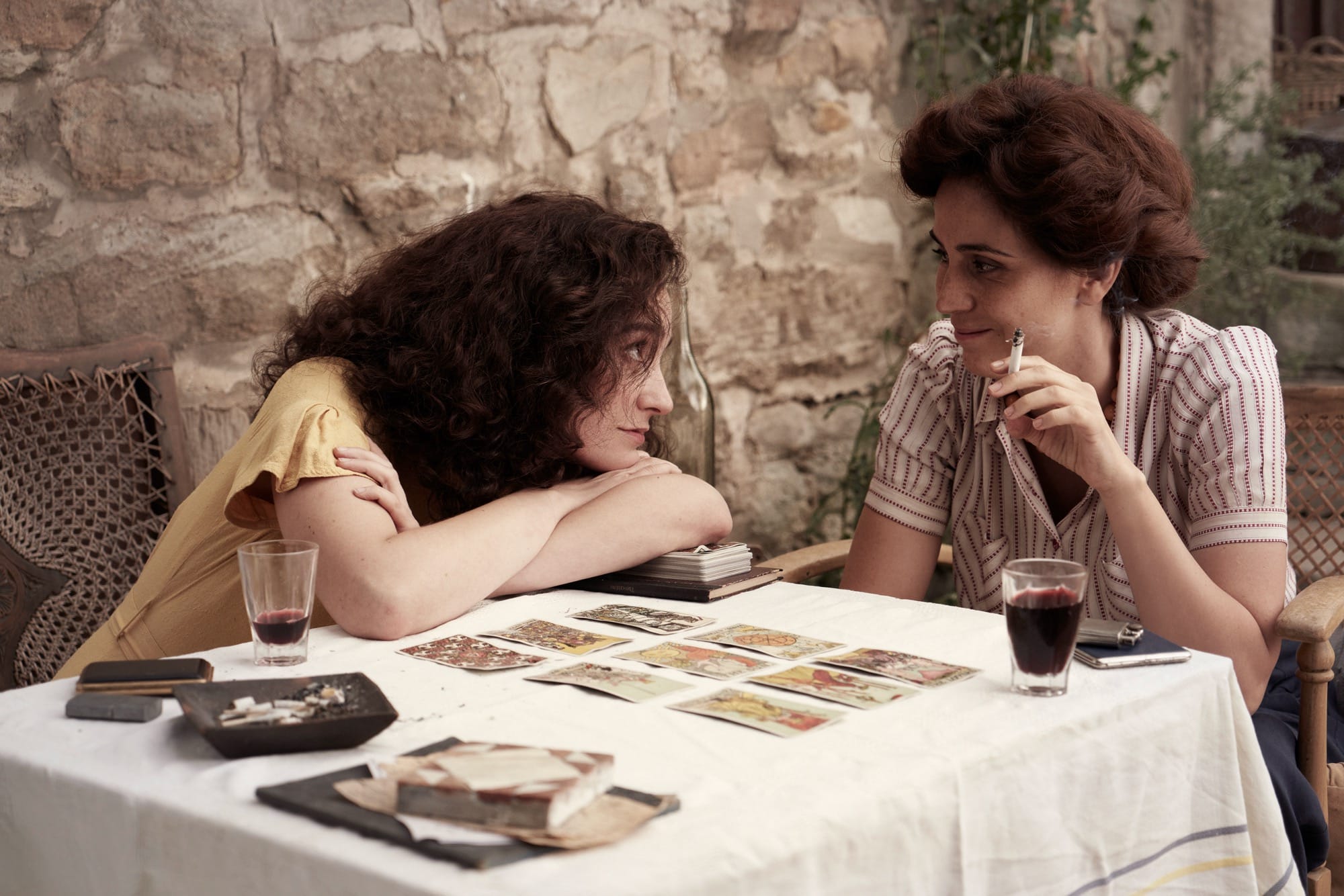 a white woman with dark curly hair looking at another woman smoking
