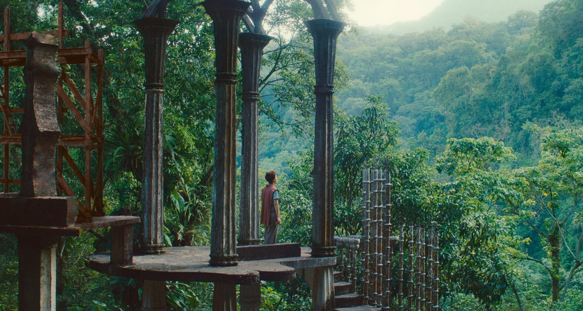 a white woman with dark curly hair standing in a beautiful architectural structure in a forest