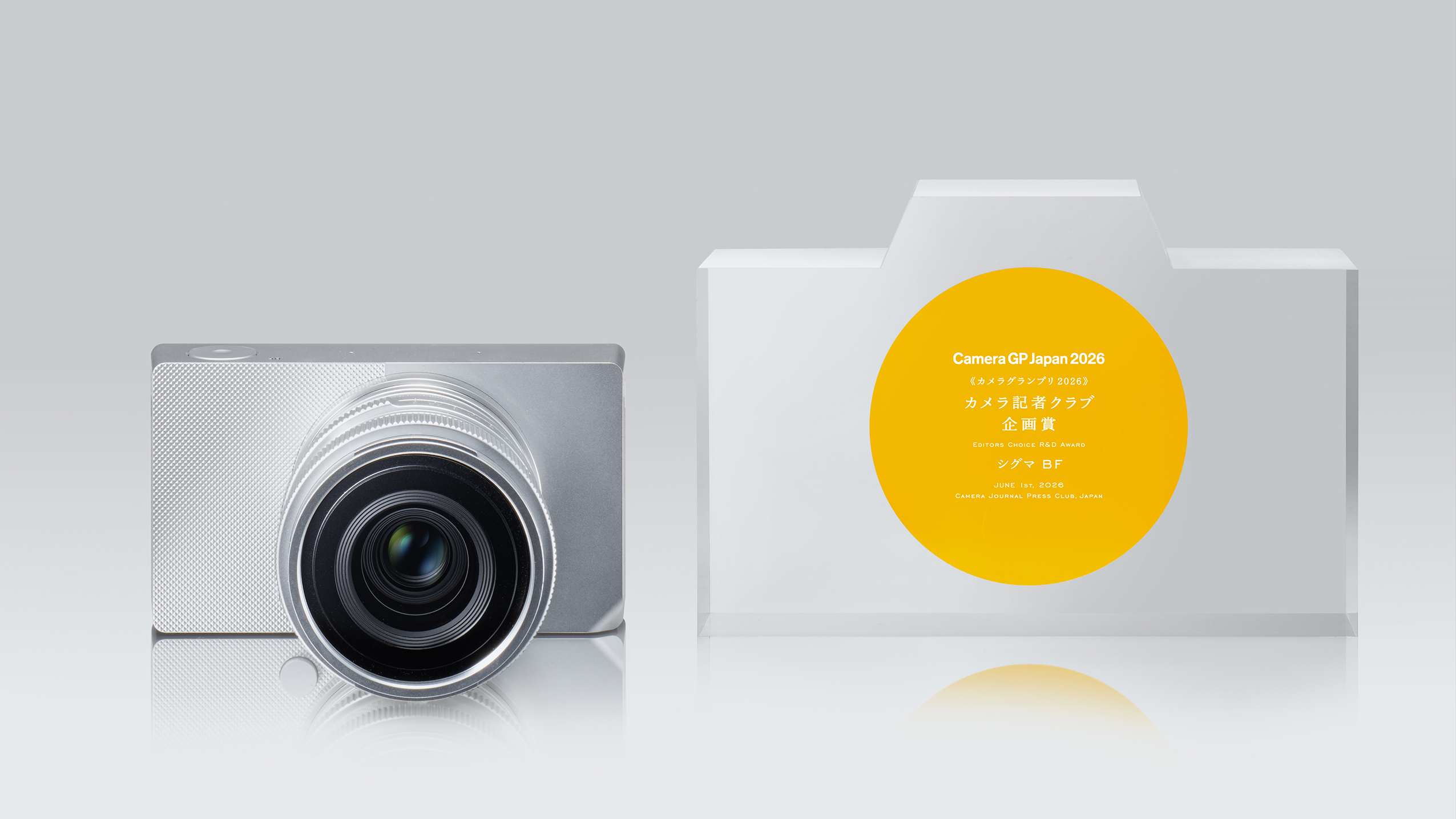 Sigma BF camera with large lens next to a camera-shaped award plaque with text and a yellow circle, against a light background