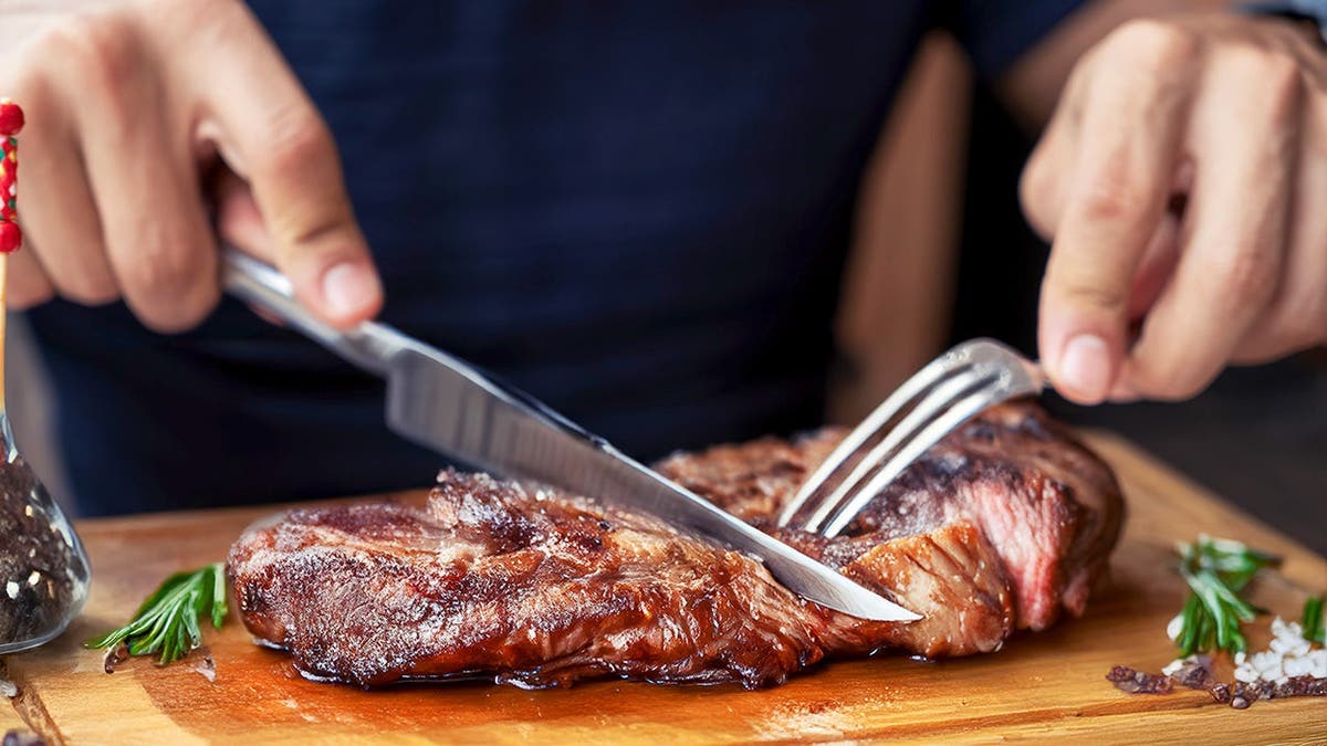 A man cuts a cooked steak with a knife and fork.