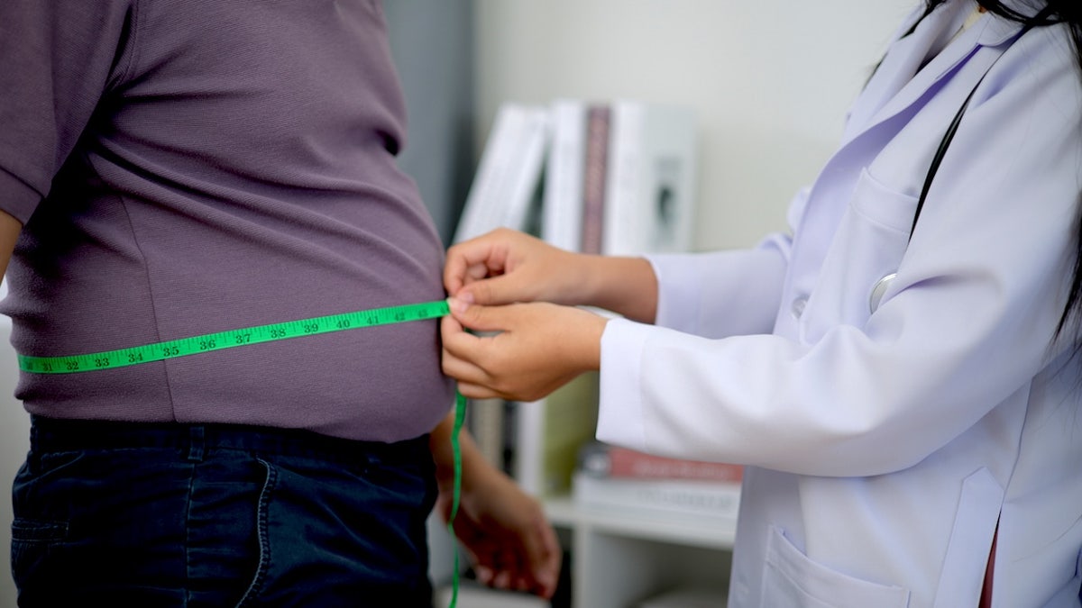 Female nutritionist measuring waist of overweight man in weight loss clinic