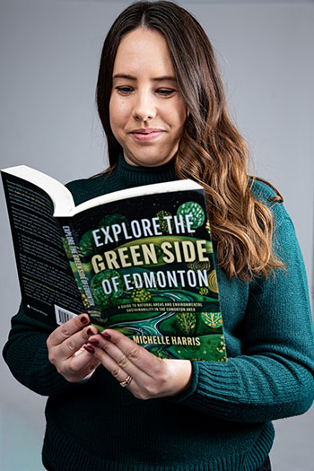 Person holding and reading the book “Explore the Green Side of Edmonton” by Michelle Harris against a plain background.