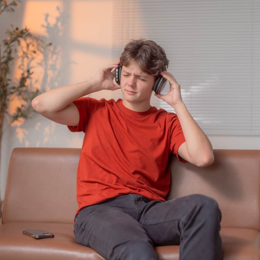 young man listening to music through headphones sitting on couch