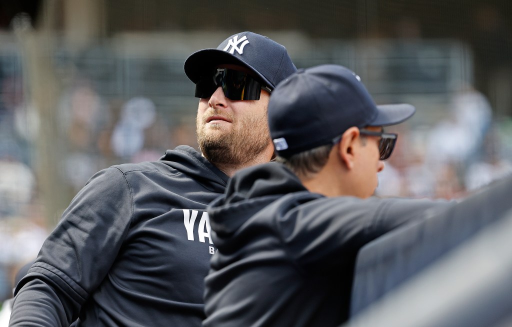 New York Yankees pitcher Gerrit Cole in a dugout, looking up while wearing sunglasses and a cap.
