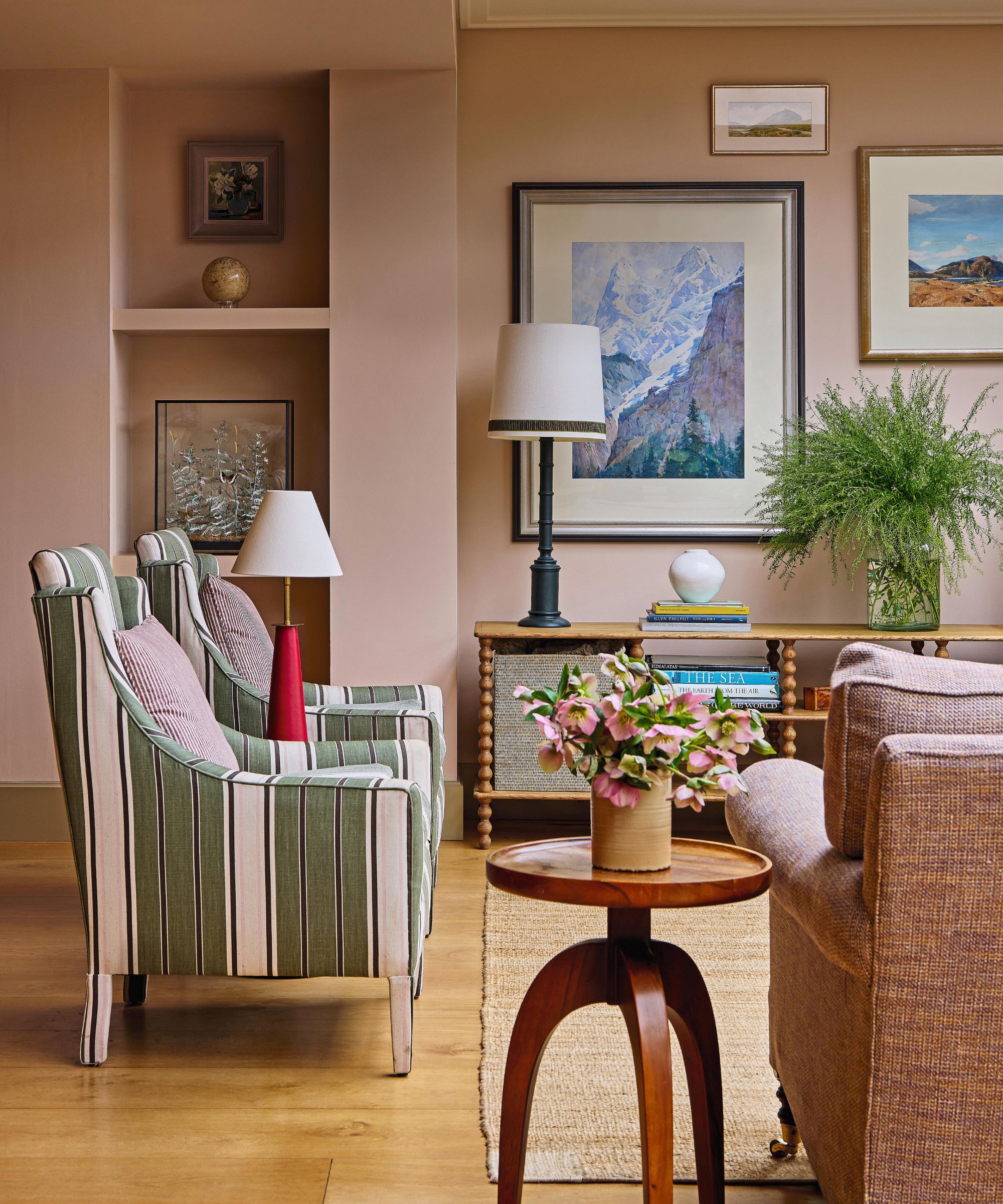 a layered pink sittin groom with large artwork, striped armchairs, wooden bobbin low shelving and mixed lamps