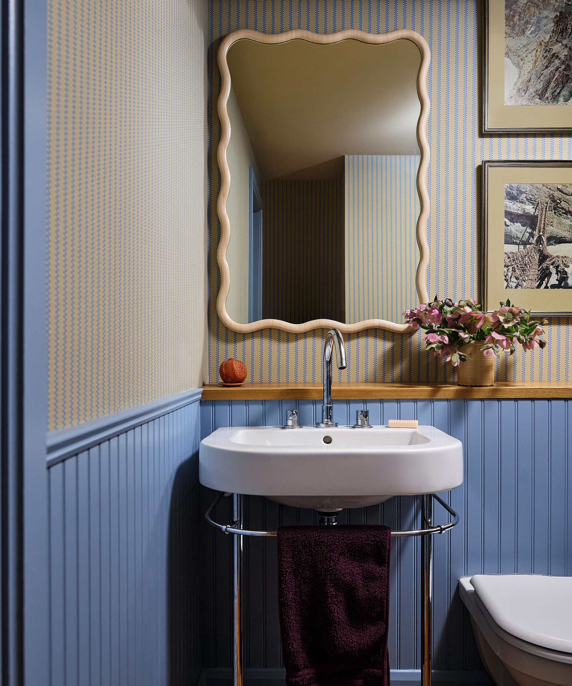 a blue paneled powder room with striped half wallpaper, a wavy mirror, small sink and toilet
