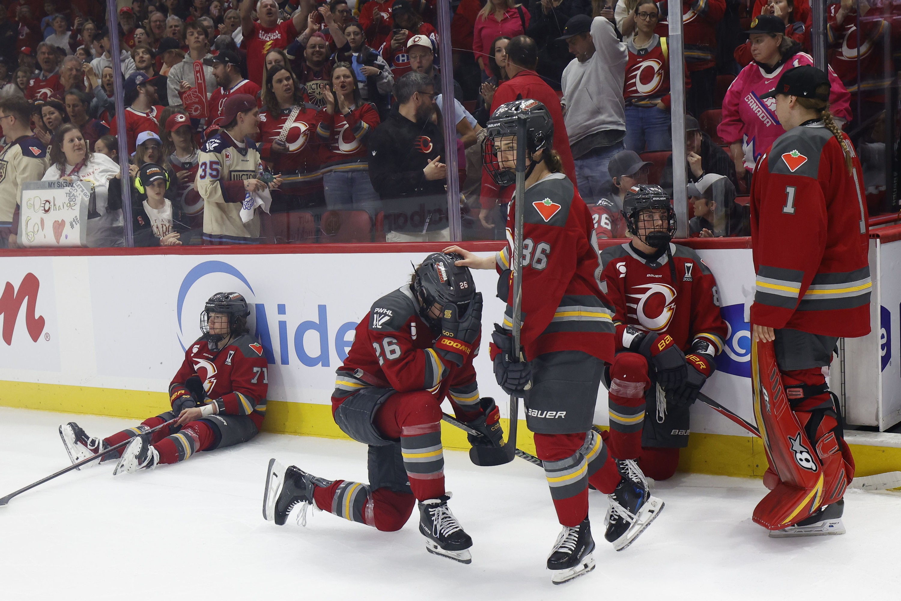 Dejected Ottawa Charge players sit, kneel and stand on the ice.