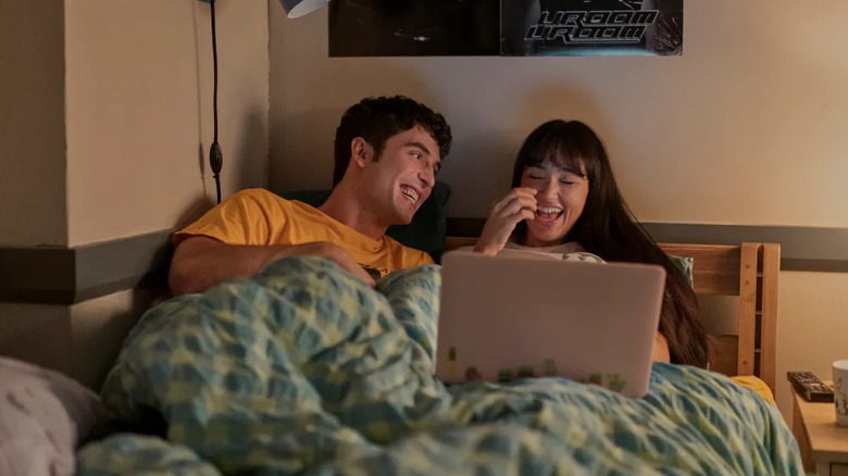 Benny and Carmen laughing and watching TV in bed on Overcompensating
