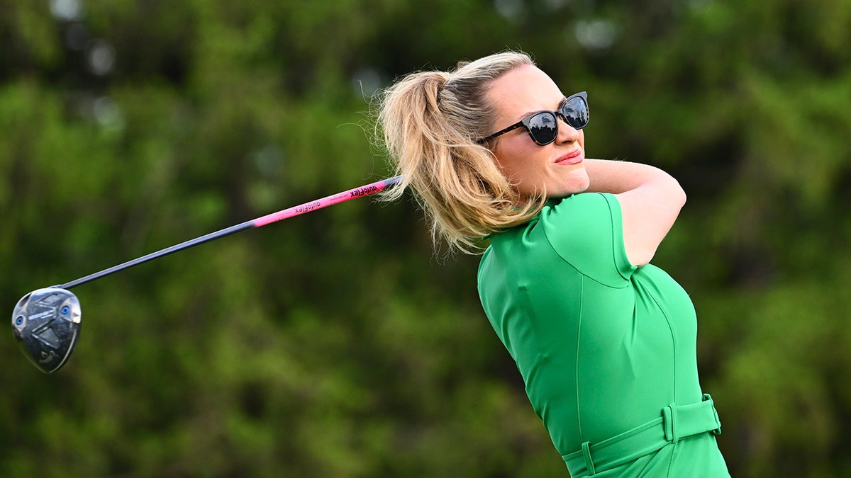 Paige Spiranac hitting a tee shot on a golf course.