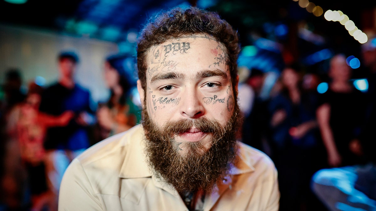 Post Malone looking directly at the camera wearing a tan shirt at the Road House world premiere.