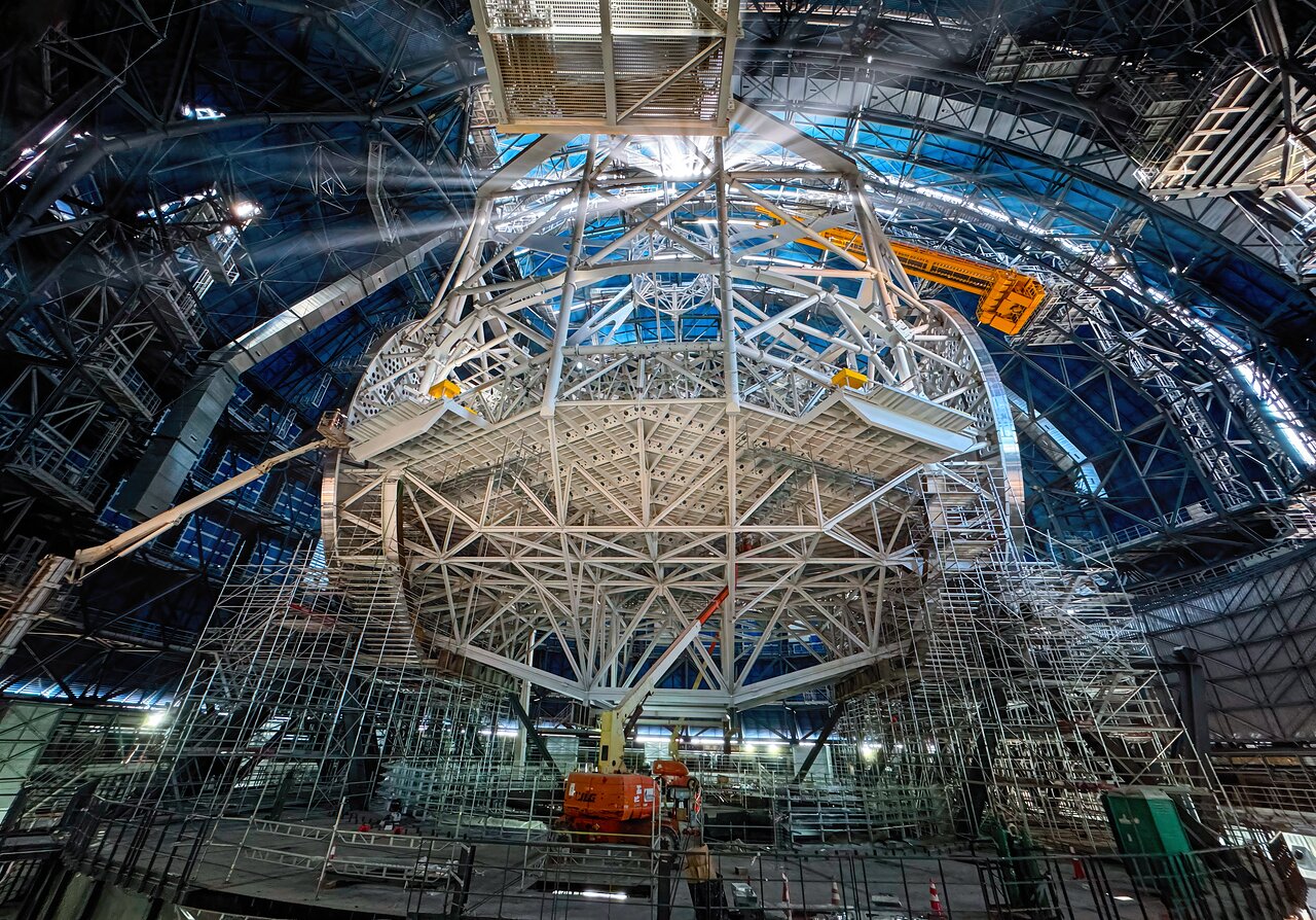 Today's Picture of the Week gives an exclusive view into the heart of ESO's Extremely Large Telescope (ELT). While the exterior appears to be almost ready for action, work is ongoing inside to complete the telescope’s structure, illuminated here by the Sun shining through the open, gigantic doors. This structure is the heart of the ELT and will host the telescope’s mirrors, which will gather the light and send it to the instruments at the sides of the telescope. At the bottom part of the structure, the cell for the main mirror is visible. The tube above connects the main mirror structure with the top ring — the spider structure that holds the secondary mirror crown. Three additional mirrors will be hosted in a tower at the centre of the main mirror, not seen here. Once the light reaches one of the platforms at the side of the telescope, an extra mirror will redirect it to one of the several scientific instruments that will analyse it. With its 39-metre-diameter, the main mirror will be the largest ever for an optical telescope, making the ELT the biggest eye on the night sky. Consequently, the technical requirements are as extreme as the ELT's name suggests. Everything about this telescope is larger than anything built before, making it the prototype that must perform perfectly, to enable us to explore the universe deeper and sharper than ever before.