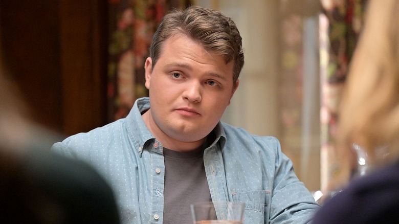 Andrew Terraciano as Sean Reagan, wearing a blue collared long-sleeved shirt over a light grey t-shirt, looking concerned while sitting at a Reagan family dinner in Blue Bloods