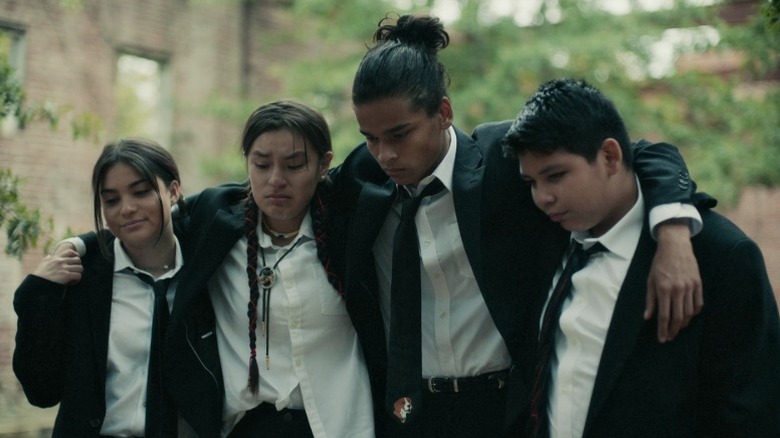 Elora (Devery Jacobs), Willie Jack (Paulina Alexis), Bear (D'Pharaoh Woon-A-Tai), and Cheese (Lane Factor) embracing and looking down mournfully on Reservation Dogs S1E1