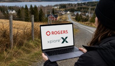 Person outdoors in a black jacket and beanie holds a laptop displaying the Rogers Xplore logo, with a rural village and lake in the background.